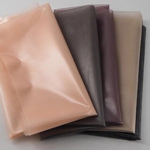 Pode incluir: Tecidos dobrados em várias cores, incluindo pêssego, castanho, roxo, bege e preto. O tecido tem uma textura brilhante e lisa, e as dobras criam sombras e reflexos.