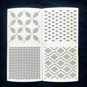Puede incluir: Cuatro cuadrados de papel blanco con diferentes patrones geométricos negros. Los patrones incluyen un diseño en forma de diamante, flechas que apuntan hacia arriba, un patrón tejido y un motivo en forma de diamante.