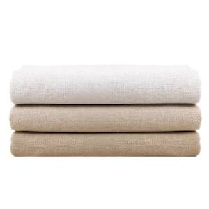May include: A stack of three folded rectangular pieces of fabric with a visible woven texture. The top piece is off-white, the middle piece is a light tan, and the bottom piece is a darker shade of tan, all featuring a consistent coarse weave.
