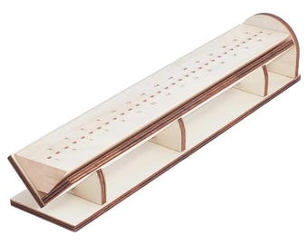 Puede incluir: Un tablero de cribbage de madera con un acabado natural. El tablero tiene una superficie de juego larga e inclinada con agujeros numerados para clavijas. Los lados y la base también son de madera, creando una estructura robusta para el juego.