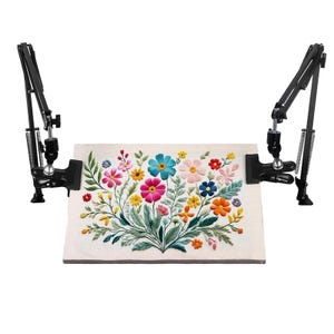 May include: A black, adjustable embroidery stand holding a floral embroidery piece. The embroidery features a variety of colorful flowers, including pink, blue, yellow, and orange, with green leaves. The stand has two adjustable arms.