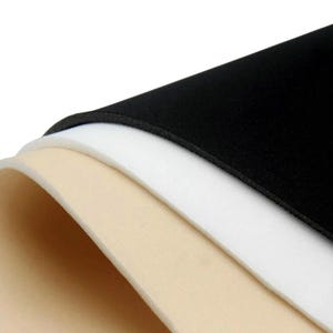 May include: A stack of three flexible, smooth sheets of foam material layered on top of each other. The top sheet is solid black, the middle sheet is solid white, and the bottom sheet is a light beige or cream color, all curved slightly.