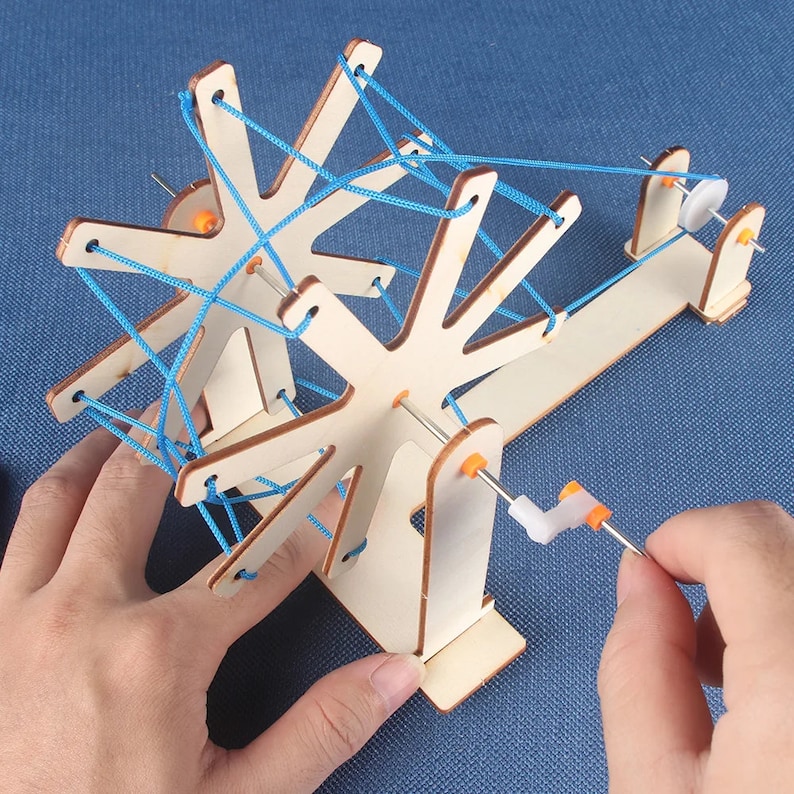 May include: A wooden toy with a spinning wheel and blue string. The wheel is connected to a crank that can be turned to make the wheel spin. The string is wrapped around the wheel and is used to create a pattern.