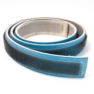 以下が含まれることがあります： 青と黒の工業用ベルトが巻かれています。表面はテクスチャ加工が施されています。ベルトは青色の裏地と黒色のブラシ状の縁があります。柔軟な素材で作られており、機械での使用を目的としています。