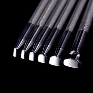 Può includere: Set di sette strumenti in metallo argentato con punte di forme diverse. Gli strumenti sono disposti in fila, con le punte rivolte verso lo spettatore.