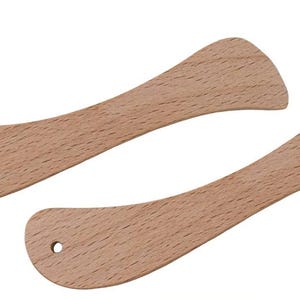 May include: Two wooden spatulas with a light brown color and a smooth finish. Each spatula has a curved handle and a rounded head with a small hole for hanging. The spatulas are designed for cooking and food preparation.