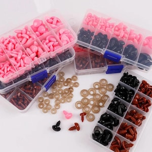 Può includere: Assortimento di materiali per l'artigianato tra cui occhi di sicurezza, pezzi per il naso e elementi di fissaggio in plastica rosa, nera e marrone. I componenti sono organizzati in scatole di plastica trasparente divise, insieme a rondelle beige.