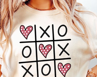 May include: A white t-shirt with a black and white noughts and crosses board design featuring three pink hearts with white polka dots. The text "SVG | PNG | EPS" is at the bottom of the shirt.