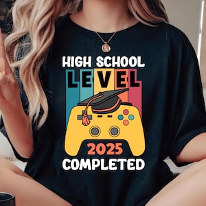 May include: Black t-shirt with a colourful graphic design. The design features the words "HIGH SCHOOL LEVEL" above a yellow video game controller with a graduation cap and the text "2025 COMPLETED".