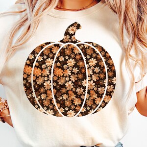 Op de afbeelding: Crèmekleurig T-shirt met een groot pompoenontwerp gevuld met een bloemenpatroon in bruin-, oranje- en crèmetinten. De pompoen heeft witte contouren. De tekst "PNG - INSTANT DOWNLOAD" staat onderaan.