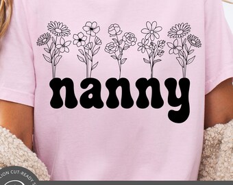 May include: Pink t-shirt with a black floral design above the word "nanny" in a bold, retro font. The shirt features a row of stylized flowers. The bottom of the image includes the text "SVG | PNG | EPS | DXF".
