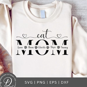 May include: A white sweatshirt with the text "cat mom" in black. The text "MOM" is large and the word "cat" is above it. Below the word "MOM" are the names "Luna", "Moon", "Charlie", "Hope", and "Sunny" in smaller text. Each name is followed by a paw print.