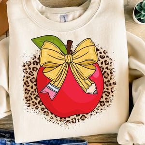 May include: A red apple with a yellow bow and two pencils, surrounded by a brown leopard print pattern.
