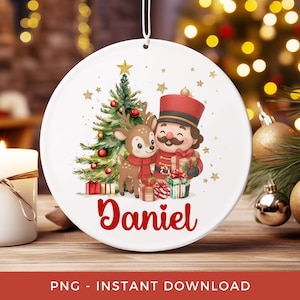 May include: White ceramic Christmas ornament featuring a festive design. The ornament showcases a Christmas tree, a deer wearing a scarf, and a nutcracker. The name "Daniel" is written in red script. Gold stars and gift boxes complete the holiday theme.