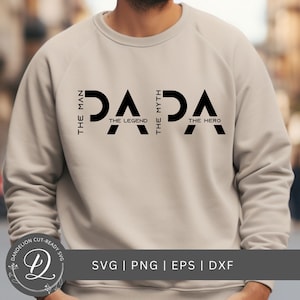 May include: A beige sweatshirt with the word "PAPA" in large black letters. The text "THE MAN", "THE MYTH", and "THE HERO" are vertically aligned on either side of the word "PAPA". The word "THE LEGEND" is below the letter "A".