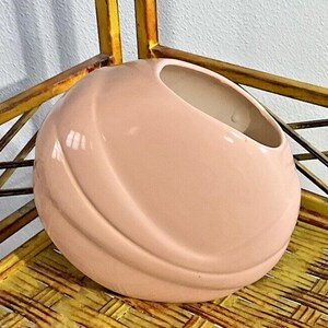 May include: A pink ceramic planter with a rounded, organic shape. The planter has a smooth, glossy finish and a wide opening at the top.