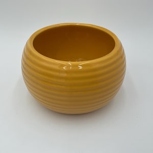 May include: A round, yellow ceramic bowl with a ribbed exterior. The bowl has a wide opening and a smooth interior. This decorative bowl is suitable for holding small items or as a decorative accent.