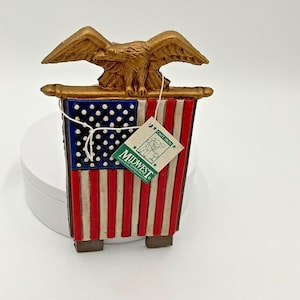 May include: A decorative American flag with a gold eagle on top. The flag features red and white stripes with a blue field of white stars. A tag from Midwest of Cannon Falls is attached.