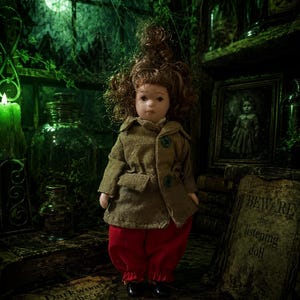 May include: A doll with curly brown hair wearing a tan collared jacket with green buttons and red trousers. The doll stands near a sign that reads BEWARE the listening doll and a paper label that reads Darkwood Apothecary Formulae for SPIRITS.