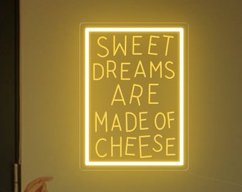 May include: A yellow neon sign with the text "SWEET DREAMS ARE MADE OF CHEESE" on a white wall. A person is standing in front of the sign, pointing at it.