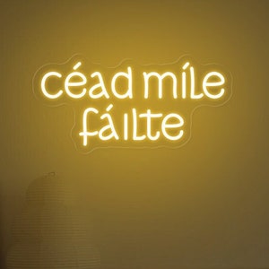 May include: A yellow neon sign with the Irish phrase "céad míle fáilte" which translates to "a hundred thousand welcomes".