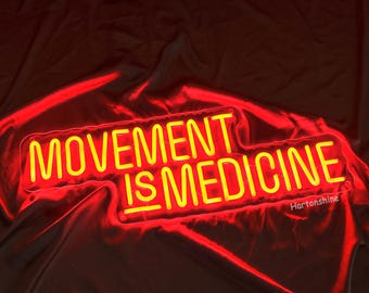 May include: Yellow neon sign with the text "Movement is Medicine" on a red fabric background.