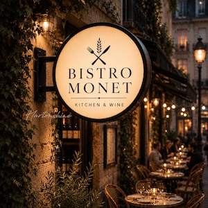 Op de afbeelding: Een rond, verlicht uithangbord voor Bistro Monet Kitchen & Wine, voorzien van een zwart icoon van een vork, een korenaar en een mes. Het bord is bevestigd aan een met klimop begroeide stenen muur boven een restaurantterras met tafels en stoelen.