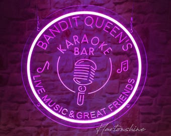 May include: A neon sign for "Bandit Queen's Karaoke Bar" with a circular design. The sign is a vibrant pink, featuring the bar's name, a microphone graphic, musical notes, and the phrases "Live Music & Great Friends."