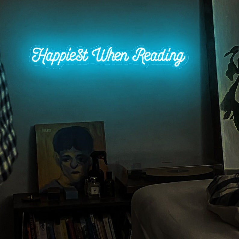 K&ouml;nnte beinhalten: Ein Neon-Schild mit dem Text "Happiest When Reading" in wei&szlig;en Buchstaben auf blauem Hintergrund.