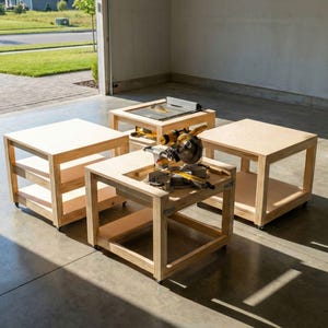 May include: Four unfinished wooden work tables of varying sizes. One table has a circular saw on top. The tables are light-coloured and have a simple, open design. The tables are on wheels.