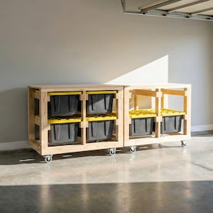 Peut inclure: Unité de rangement en bois avec deux sections, chacune avec deux étagères. Chaque étagère contient un bac en plastique noir avec un couvercle jaune. L'unité est sur roulettes et le bois a une finition naturelle. L'unité est dans un garage.