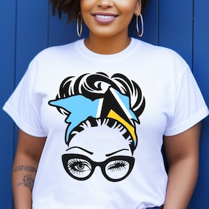 May include: White t-shirt with a graphic of a woman's face with a bun, wearing glasses and a headband with the colors of the Bahamian flag.