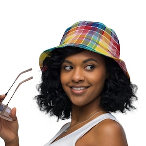 以下が含まれることがあります： 赤、黄、緑、青の四角模様のカラフルなチェック柄バケットハット。メガネを持った人がかぶっています。つばが広く、丸みを帯びたクラウンの帽子です。背景は白です。