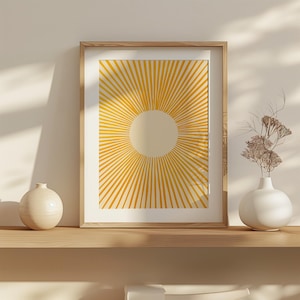 Puede incluir: Una impresión enmarcada con un diseño de sol amarillo sobre un fondo crema. El sol está formado por finas líneas amarillas que irradian desde un círculo central.