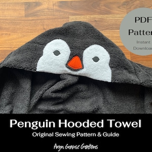 Puede incluir: Una toalla con capucha negra con una aplicación de cara de pingüino blanca. La toalla está hecha para niños y tiene una capucha con una cara de pingüino. El texto "Penguin Hooded Towel" y "Original Sewing Pattern & Guide" está impreso en la parte inferior de la imagen. El texto "Argn Grause Creations" está impreso en cursiva en la parte inferior de la imagen.
