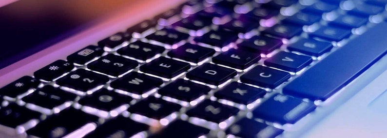 May include: A close-up of a black laptop keyboard with white keys and a blue light reflecting off the keys.