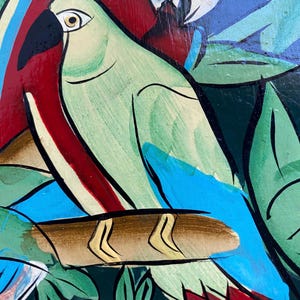 May include: A painting of two parrots perched on a branch. The parrot on the left is green with blue wings and a yellow beak. The parrot on the right is red with blue wings and a white head. The background is a dark green with leaves and flowers.