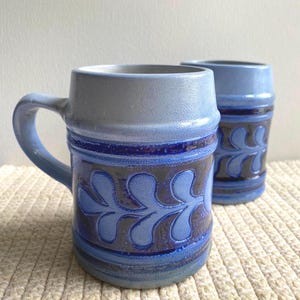 Puede incluir: Dos tazas de cerámica azul y blanca con un diseño de hojas. Las tazas tienen un acabado esmaltado y están decoradas con un patrón de hojas azul y blanco.
