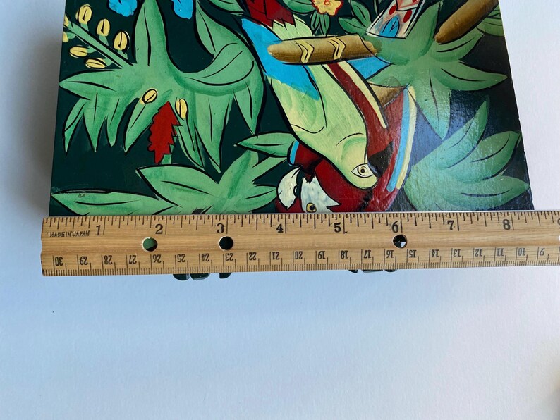 May include: A hand-painted wooden box with a colorful design of parrots and tropical plants. The box is approximately 8 inches long.
