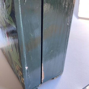 May include: A green wooden box with a hinged lid and painted floral details. The box is closed and the lid is slightly ajar.