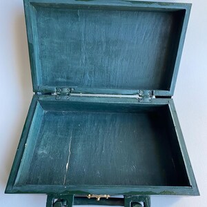 May include: A dark green wooden box with a hinged lid and a metal handle. The box is empty and open.
