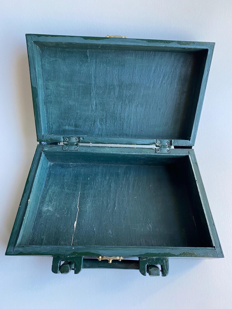 May include: A dark green wooden box with a hinged lid and a metal handle. The box is empty and open.