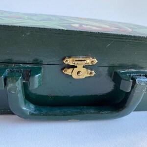 May include: A dark green wooden box with a hinged lid and a brass latch. The box has a painted design on the top and a handle on the front.