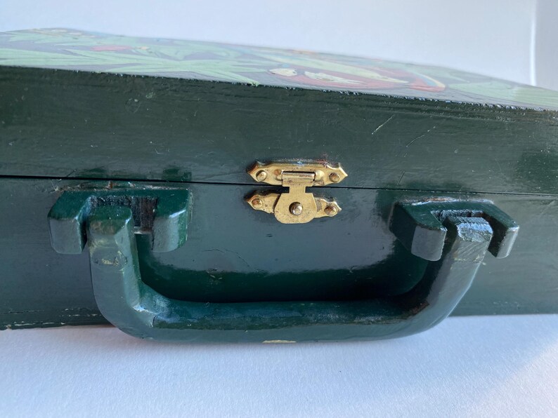 May include: A dark green wooden box with a hinged lid and a brass latch. The box has a painted design on the top and a handle on the front.