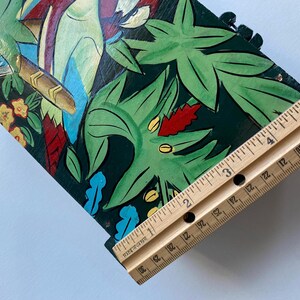May include: A wooden box with a painted design of tropical leaves and birds. The box is approximately 3 inches wide.