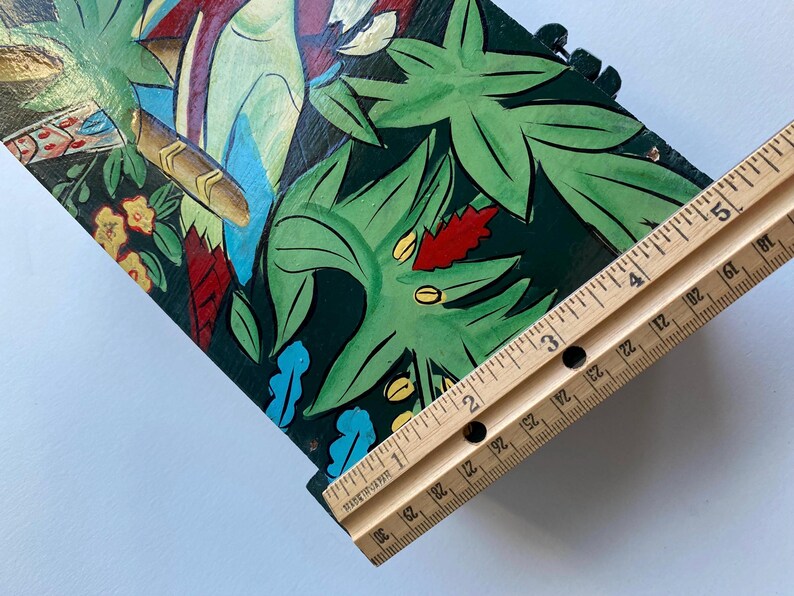 May include: A wooden box with a painted design of tropical leaves and birds. The box is approximately 3 inches wide.