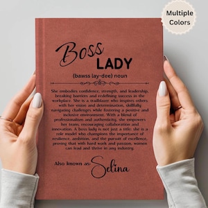 Puede incluir: Un cuaderno de color terracota sostenido por una persona. La portada presenta las palabras "Boss Lady" en una escritura elegante, junto con una definici&oacute;n y un texto inspirador. El cuaderno est&aacute; personalizado con el nombre "Selina".