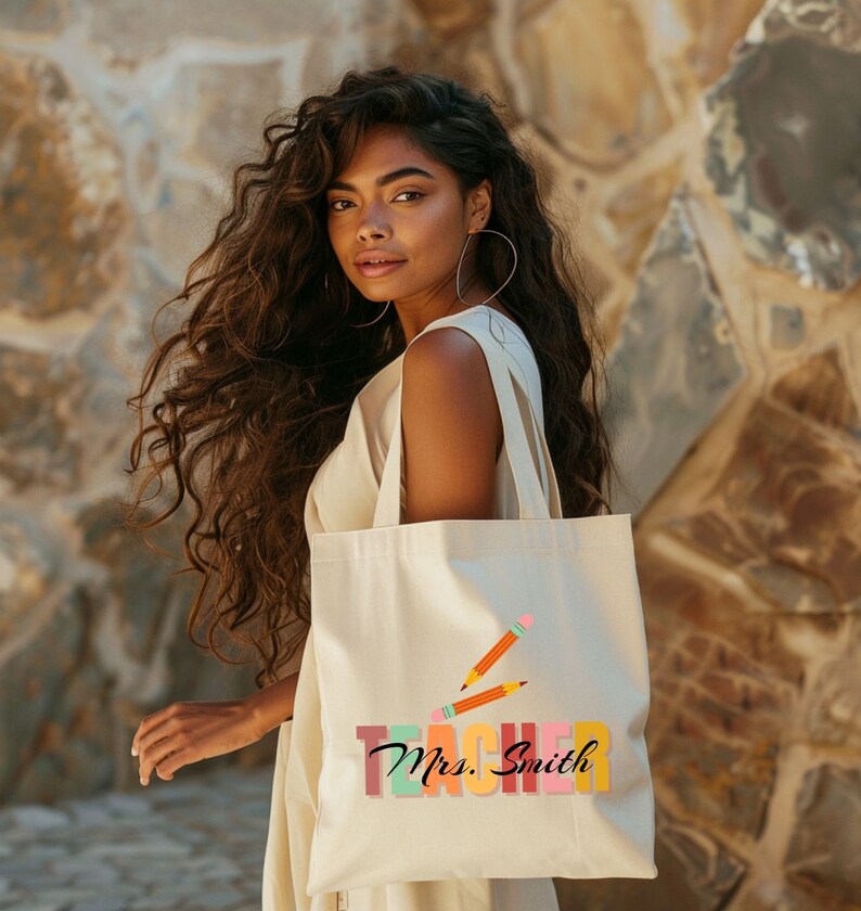 Pu&ograve; includere: Una borsa tote beige con un design "Teacher" colorato e il nome "Mrs. Smith" in corsivo. La borsa presenta due matite arancioni con gomme rosa.