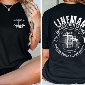 Puede incluir: Camiseta negra con un gr&aacute;fico blanco de un pu&ntilde;o sosteniendo un rayo y el texto "Lineman". La parte posterior de la camiseta tiene un gr&aacute;fico blanco de un lineman escalando un poste de energ&iacute;a con el texto "Lineman Rain Shine Sleet or Snow Powerful Linemen Keep the Lights On Climbing Poles Defying Gravity Company Name".