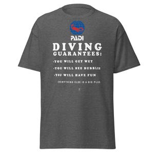 以下が含まれることがあります： PADIのロゴと「DIVING GUARANTEES: YOU WILL GET WET, YOU WILL SEE BUBBLES, YOU WILL HAVE FUN, EVERYTHING ELSE IS A BIG PLUS」の文字が入った濃いグレーのTシャツ。Tシャツはクルーネックで半袖です。